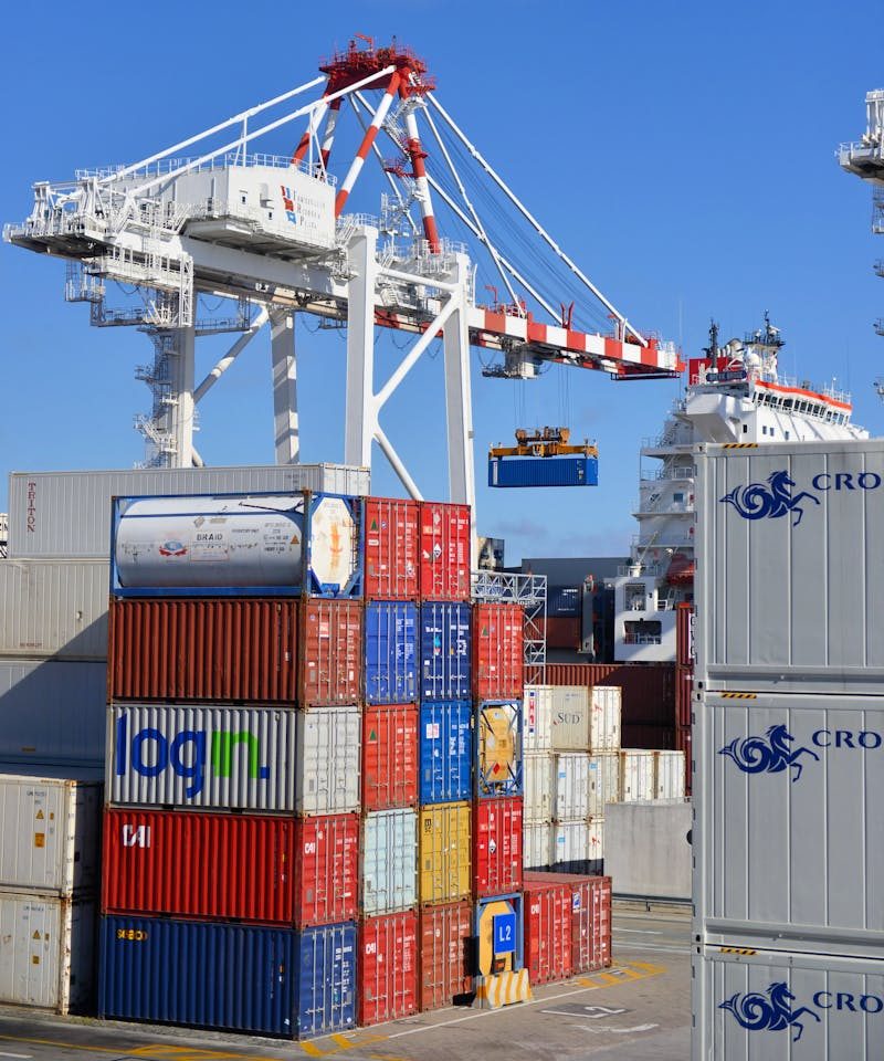Colorful shipping containers stacked in a busy port with cranes overhead.